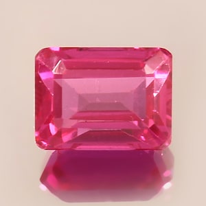 Puede incluir: Una gema rosa vibrante con un corte esmeralda. La gema está facetada y tiene un alto pulido.