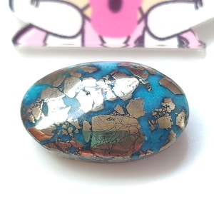 Pode incluir: Um close-up de uma gema oval cabochão turquesa e ouro. A gema tem um padrão único de manchas douradas em toda a turquesa.