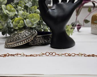 Könnte beinhalten: Ein Kupferarmband mit weißen Perlen. Das Armband ist aus Draht gefertigt und hat ein zartes, filigranes Design.