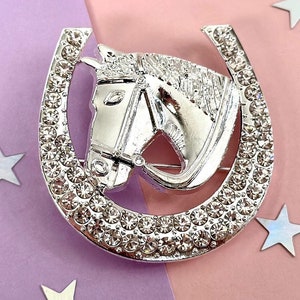 May include: Silver horseshoe brooch with a horse's head design, decorated with clear rhinestones.