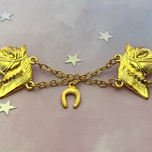 May include: Gold-toned horse head brooch with a horseshoe charm and a chain connecting the two horse heads.