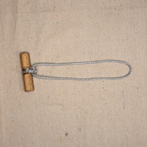 Puede incluir: Un botón de madera con una cuerda gris enhebrada a través de él. El botón es de forma simple, cilíndrica con extremos redondeados.