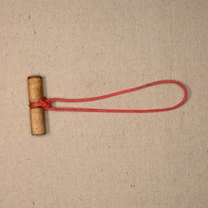 Puede incluir: Una cuerda roja atada alrededor de una clavija de madera. La cuerda está anudada alrededor de la clavija y atada en un nudo.