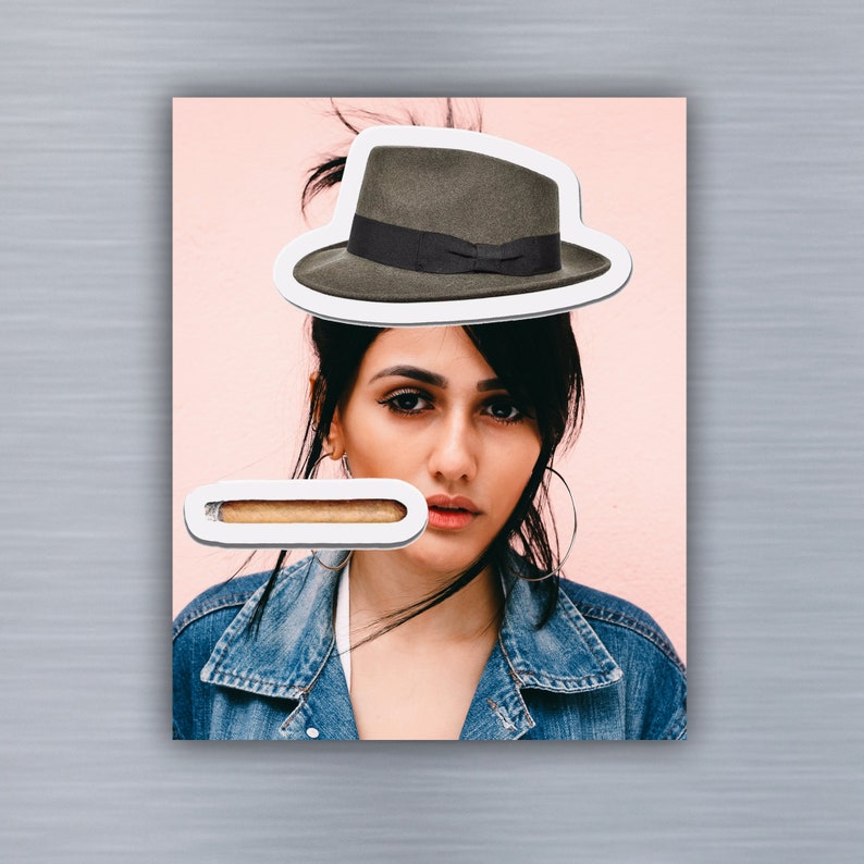 May include: A woman with dark hair wearing a denim jacket and a brown fedora. She is looking at the camera. A white rectangle with a brown bar inside is in the foreground.