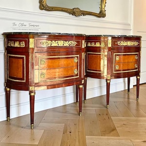 May include: Pair of antique mahogany sideboards with marble tops. Each sideboard features two drawers and a cabinet door, accented with gold trim and hardware. The curved design and elegant legs add to the classic aesthetic. The text "The Other Treasure" is visible.