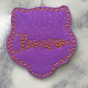 May include: Purple felt patch with an orange embroidered outline and the name "Clemson" in orange thread.
