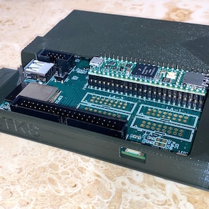 May include: A green 3D printed case with a circuit board inside. The board has a USB port, a micro SD card slot, and a header with many pins. The case has the text "EBTKS" printed on the side.