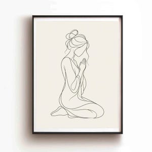 Puede incluir: Una lámina de arte mural enmarcada con un dibujo de línea continua negra de una persona arrodillada con las manos juntas en posición de oración. La figura tiene el cabello recogido en un moño sobre un fondo beige claro.