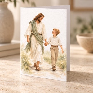 Könnte beinhalten: Eine Grußkarte mit einer Aquarellillustration einer langhaarigen Figur in weißem Gewand und grünem Schal, die Hand in Hand mit einem kleinen Kind in hellem Hemd und beigefarbener Hose auf einem Pfad durch ein Feld mit kleinen weißen Blumen geht.