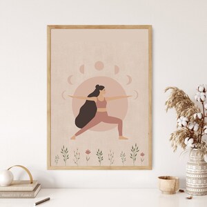 Pode incluir: Uma ilustração digital de uma mulher em uma pose de ioga rosa com um design de fase lunar rosa e branco no fundo. A ilustração é emoldurada em uma moldura de madeira clara.