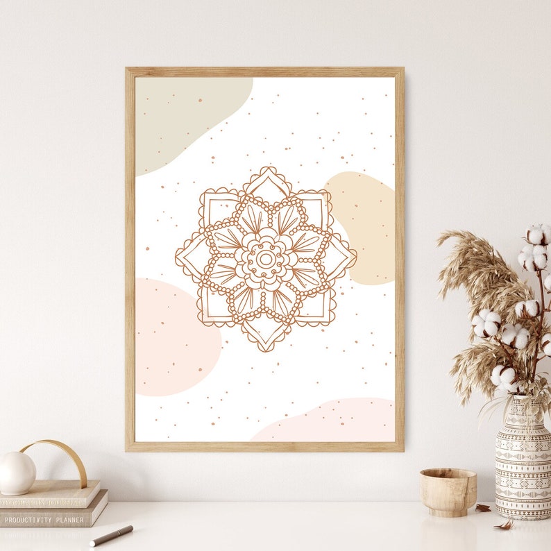 Op de afbeelding: Een ingelijste kunstdruk met een bruin mandala-ontwerp op een witte achtergrond, aangevuld met abstracte beige en perzikvormen. Het kunstwerk wordt gepresenteerd in een licht houten frame. Minimalistische, bohemien esthetiek voor interieurdecoratie.