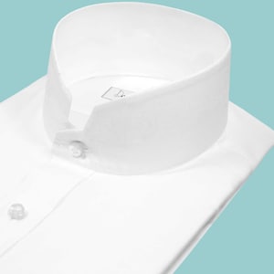 Könnte beinhalten: Ein makelloses weißes Hemd mit einem hohen, abgerundeten Kragen und einer Knopfleiste. Das Hemd hat ein klassisches Design, ideal für formelle oder geschäftliche Anlässe. Der Kragen hat eine einzigartige Form.