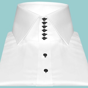 May include: A crisp white dress shirt with a high collar and black buttons. The shirt is neatly folded, showcasing its tailored design. The collar features a series of small, decorative buttons, adding a touch of elegance to the classic garment.