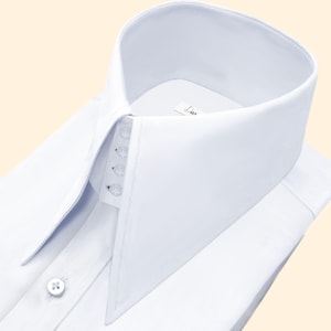 Può includere: Una camicia bianca impeccabile con un colletto alto e appuntito. La camicia presenta una chiusura con bottoni e un design classico, ideale per occasioni formali. Il colletto è rigido e ben definito, aggiungendo eleganza.