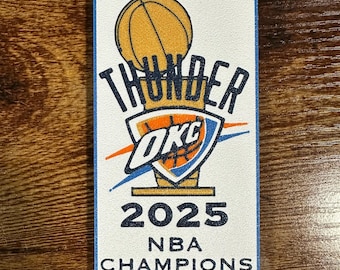 May include: A rectangular patch with a blue border features the text "THUNDER OKC" above "2025 NBA CHAMPIONS." The design includes a basketball, a trophy, and the team's logo in orange, blue, and white.