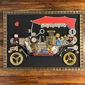 Könnte beinhalten: Ein gerahmtes Mixed-Media-Wandbild, das aus verschiedenen Fundstücken zu einem alten Automobil zusammengesetzt ist. Die Komposition besteht aus Messingrädern, einem roten Stoffdach mit Spitzenbesatz, Schlüsseln, einer Zündkerze und diversen Metallteilen.
