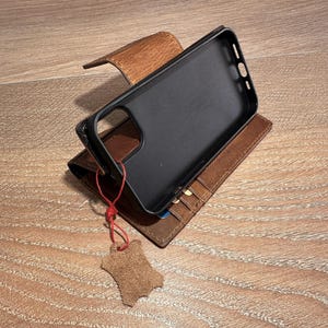 A black smartphone case is placed on top of a brown leather wallet, which is resting on a wooden surface.