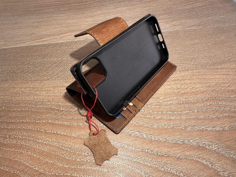 A black smartphone case is placed on top of a brown leather wallet, which is resting on a wooden surface.