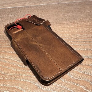 A brown leather wallet or fanny pack is placed on a wooden surface.