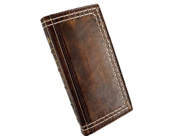 May include: A brown leather journal with white stitching and gold accents. The journal has a distressed look and is closed.