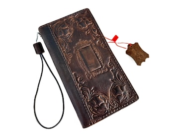 May include: A dark brown leather wallet with an embossed floral design and a rectangular frame. The wallet has a wrist strap and a leather tag attached with a red string. The overall design is vintage and detailed.