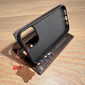 a black phone case placed on top of a brown leather wallet, which is resting on a wooden surface.