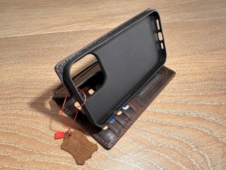 a black phone case placed on top of a brown leather wallet, which is resting on a wooden surface.
