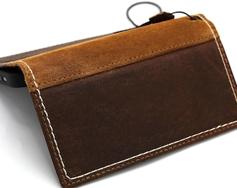 May include: A brown leather phone case with a contrasting tan suede flap. The case is stitched with white thread and has a black lanyard attached. The phone is partially visible inside the case.