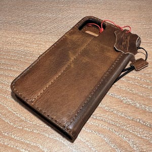 A brown leather wallet or case with a red string attached, resting on a wooden surface.