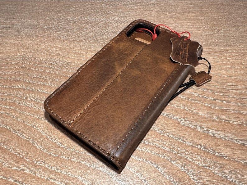 A brown leather wallet or case with a red string attached, resting on a wooden surface.