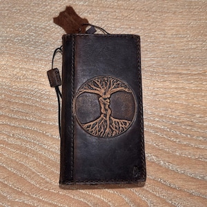 A brown leather wallet or book cover with a tree design on it, resting on a wooden surface.
