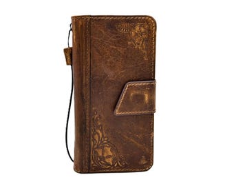 May include: A brown leather phone case with a distressed finish. The case features embossed floral and geometric designs, a magnetic flap closure, and a wrist strap. The case is designed to protect a phone.