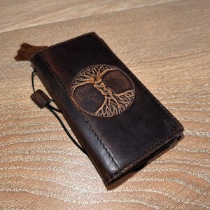 A brown leather wallet or book cover with a tree design embossed on it, resting on a wooden surface.