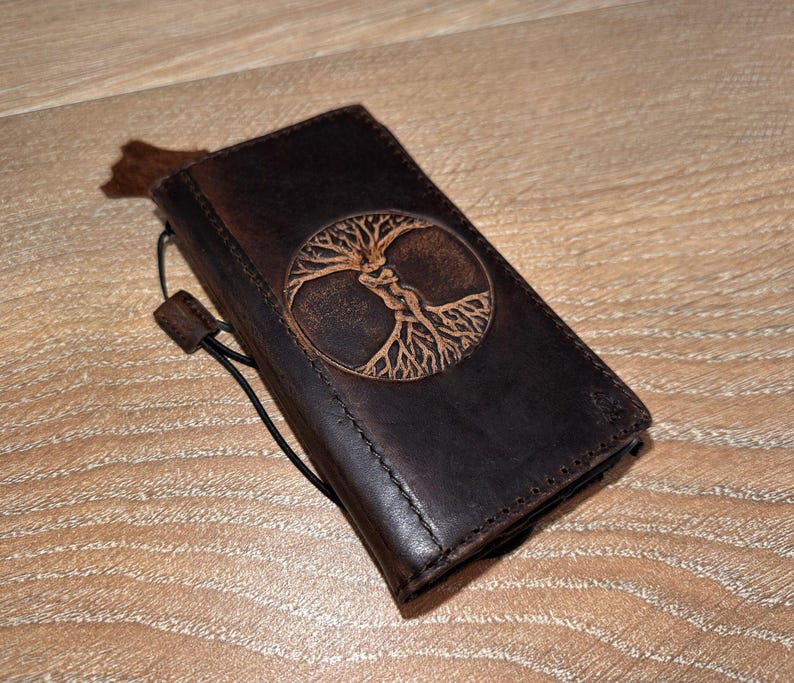 A brown leather wallet or book cover with a tree design embossed on it, resting on a wooden surface.
