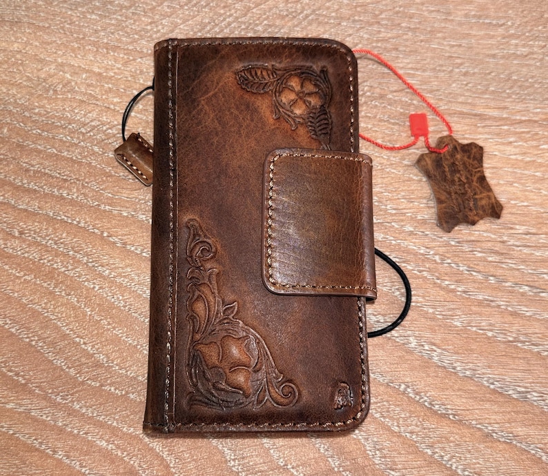 A brown leather wallet with embossed floral designs and a red tag attached to it, placed on a wooden surface.