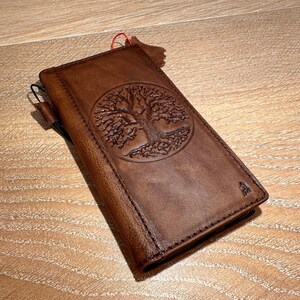 A brown leather wallet or book with a tree design embossed on the cover, resting on a wooden surface.