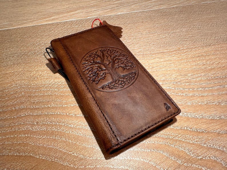 A brown leather wallet or book with a tree design embossed on the cover, resting on a wooden surface.
