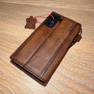 A brown leather wallet or case with a zipper closure and a small red tag attached to it, resting on a wooden surface.