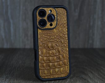 Pode incluir: Uma capa de telefone preta com uma parte traseira de couro marrom com relevo de crocodilo. A capa tem uma protuberância de câmera elevada com três lentes.