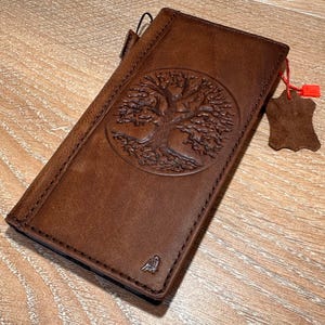 A brown leather wallet or book with a tree design embossed on the cover, resting on a wooden surface.