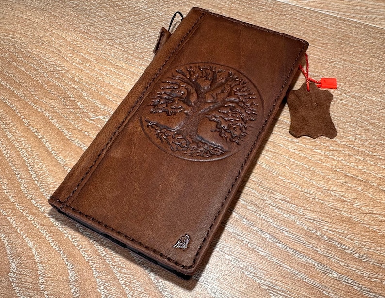 A brown leather wallet or book with a tree design embossed on the cover, resting on a wooden surface.