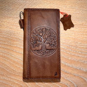 A brown leather wallet or card with a tree design embossed on it, placed on a wooden surface.