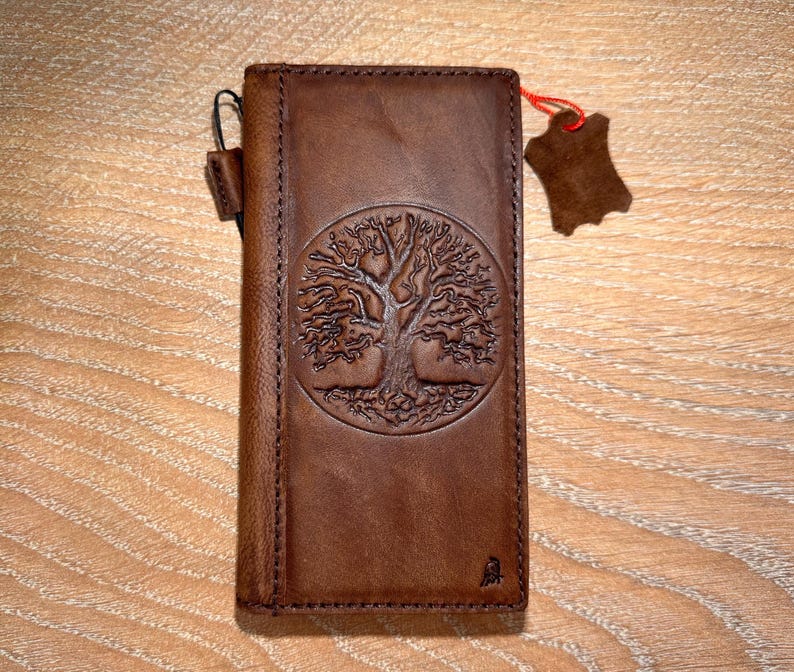 A brown leather wallet or card with a tree design embossed on it, placed on a wooden surface.