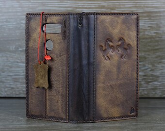 May include: A brown leather phone case with a stitched design and a small leather tag. The case has a flap that folds over the phone and a small pocket on the back.