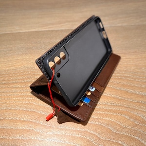 A black smartphone case is placed on top of a brown leather wallet, which is resting on a wooden surface.