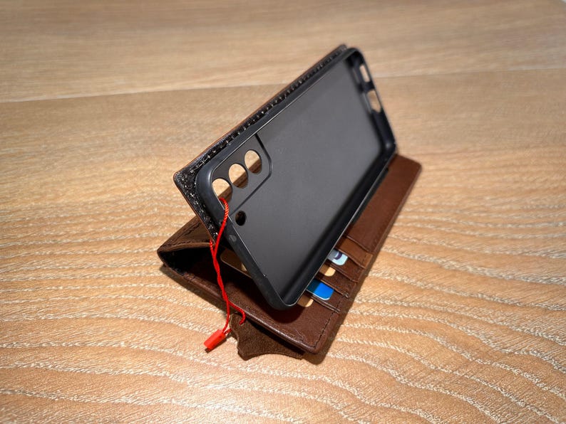 A black smartphone case is placed on top of a brown leather wallet, which is resting on a wooden surface.