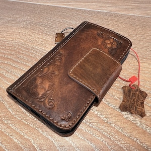 A brown leather wallet or fob case is placed on a wooden surface, with a red string attached to it.