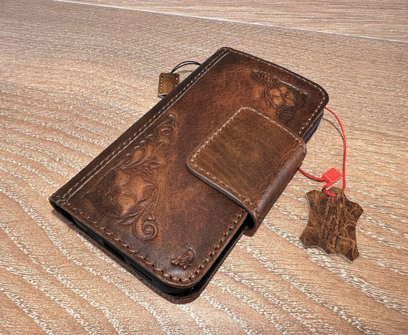 A brown leather wallet or fob case is placed on a wooden surface, with a red string attached to it.