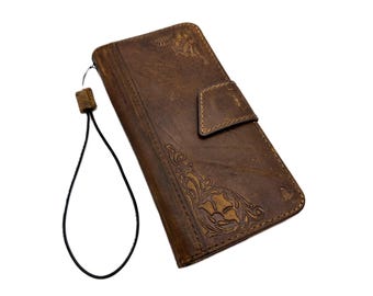 May include: Brown leather phone case with a floral embossed design and a magnetic flap closure. The case has a wrist strap attached. The leather has a distressed look.