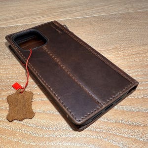 A brown leather wallet is placed on a wooden surface, with a red tag attached to it.